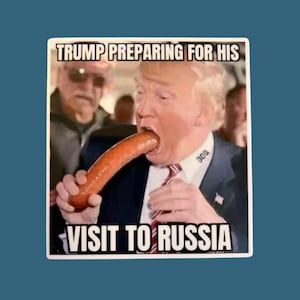 May include: A sticker featuring a meme of a man in a suit eating a sausage. The text at the top reads "TRUMP PREPARING FOR HIS" and the text at the bottom reads "VISIT TO RUSSIA". The background is blurred.