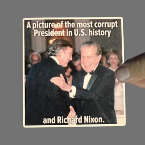 May include: A sticker featuring a photograph of two men in suits shaking hands. The sticker has the text "A picture of the most corrupt President in U.S. history and Richard Nixon."