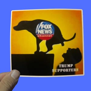 May include: A sticker with a black silhouette of a dog pooping on a person. The dog's body contains the Fox News Channel logo. The words "TRUMP SUPPORTERS" are below the person's silhouette. The background is yellow and orange.