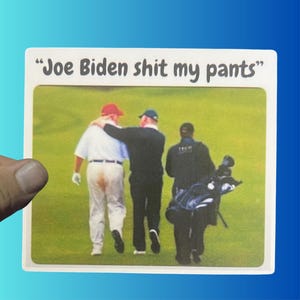 May include: A white card with the text "Joe Biden shit my pants" printed in black. The card features a photo of three men on a golf course. The man in the middle is wearing a red hat and a white shirt. The man on the left is wearing a white shirt and brown pants. The man on the right is wearing a black shirt and black pants.
