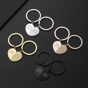 May include: A selection of keyrings with heart-shaped pendants. Each heart is split in two, with the text "YOUR MESSAGE" engraved on each half. Keyrings are in silver, gold, rose gold, and black.