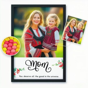 May include: Framed print featuring a mother and child in traditional red and white embroidered outfits. The print includes a smaller image and a circular display of pink and yellow candies. The text reads "Mom" and "You deserve all the good in the universe."