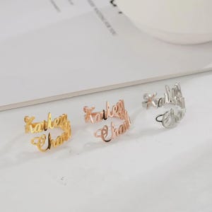 May include: Three open-style rings, each featuring the name "Kailey Chan" in a cursive font. One ring is gold, one is rose gold, and the third is silver. The rings are displayed on a white surface.