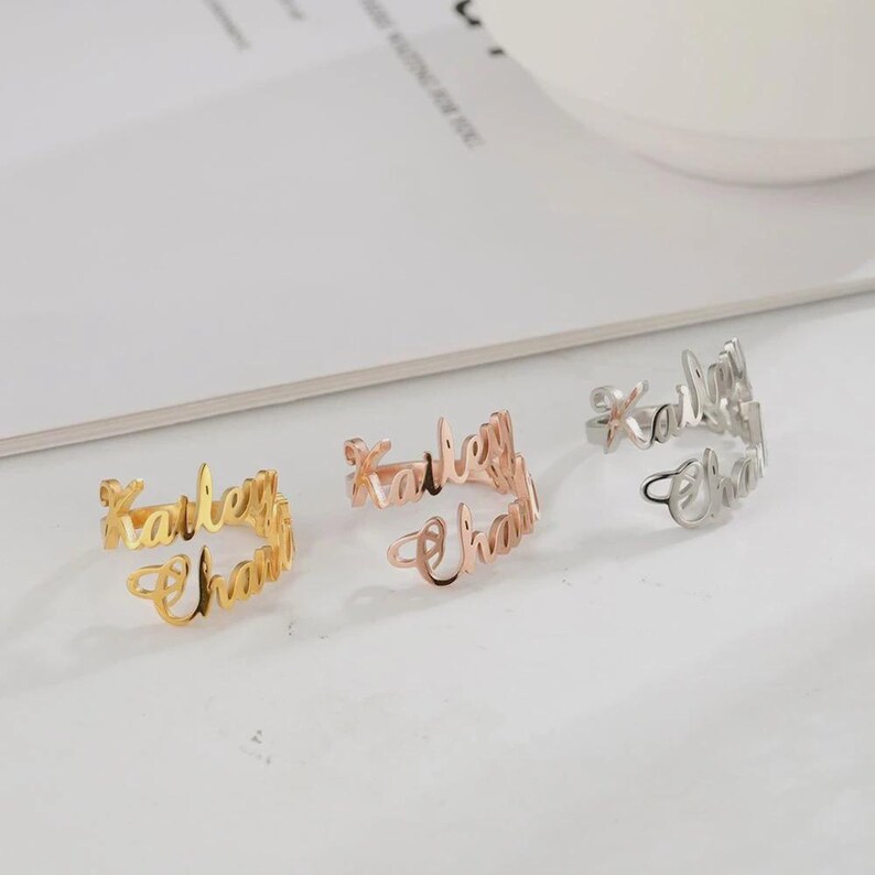 May include: Three open-style rings, each featuring the name "Kailey Chan" in a cursive font. One ring is gold, one is rose gold, and the third is silver. The rings are displayed on a white surface.