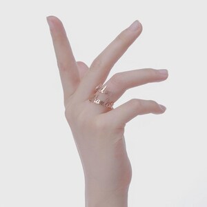 May include: A rose gold double-band ring with the names "Avery" and "Charlotte" in a delicate script. The ring is displayed on a hand against a soft, neutral background. The ring is a personalized jewelry item.