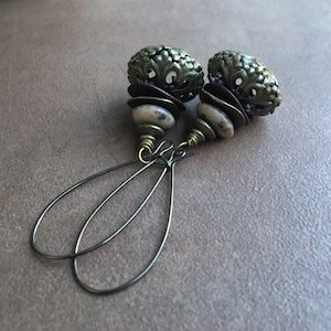 May include: A pair of earrings with a brown and white stone bead and a green metal filigree charm. The earrings have a simple wire loop design.
