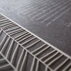 May include: A close-up of a gray, textured, rectangular surface with the words "EMOTIONAL", "ADVENTURE", "COMMITTED TO", "TOLERANCE, ART, MUSIC", "ANEW; MAY WE BE BETTER", and "VIDAL" printed in white.