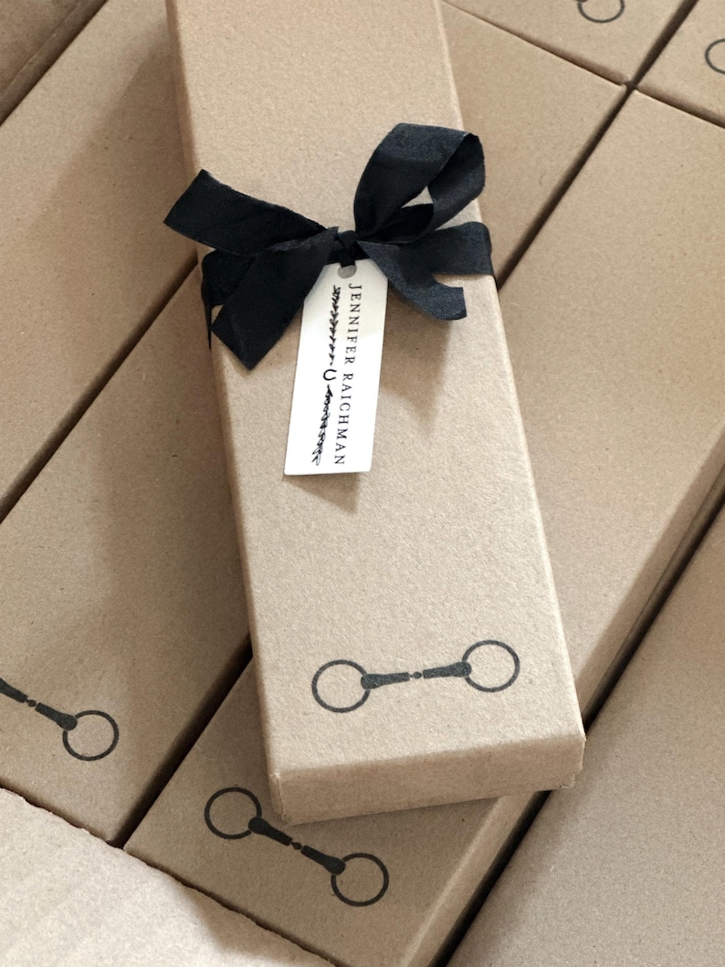 May include: A stack of brown cardboard boxes with black ribbon and a tag that reads "Jennifer Raichman". The boxes have a black silhouette of a horse bit on the front.