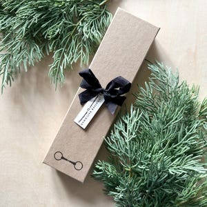 May include: A brown gift box with a black ribbon and a small tag that says "Jennifer & Bachman". The box is decorated with a black horseshoe logo.