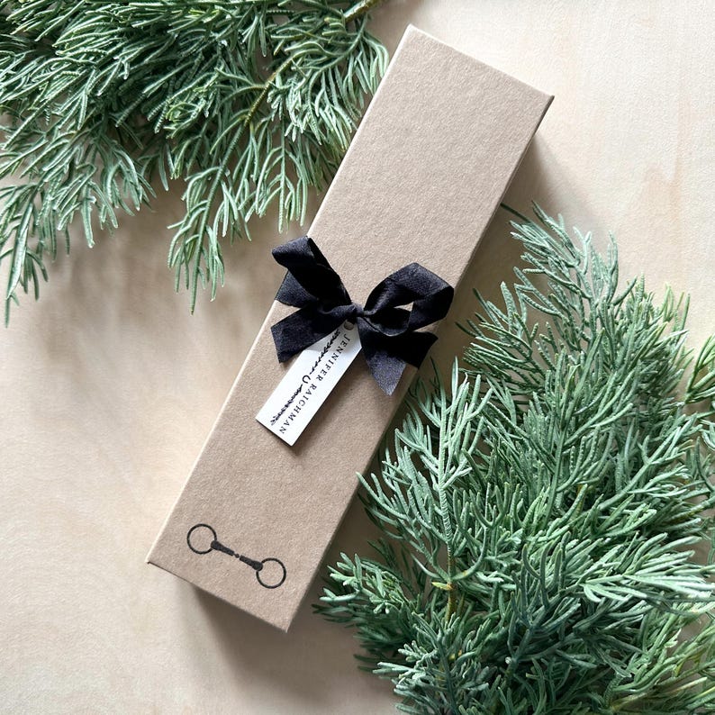 May include: A brown gift box with a black ribbon and a small tag that says "Jennifer & Bachman". The box is decorated with a black horseshoe logo.
