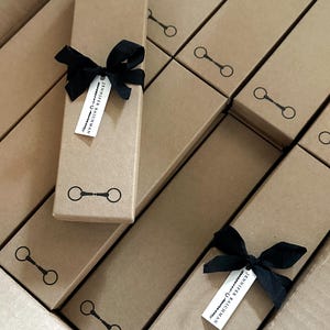 May include: A stack of brown cardboard boxes with black ribbon bows and a small white tag with the text "Jennifer Rauchman" on each box. The boxes have a black horseshoe design printed on the front.