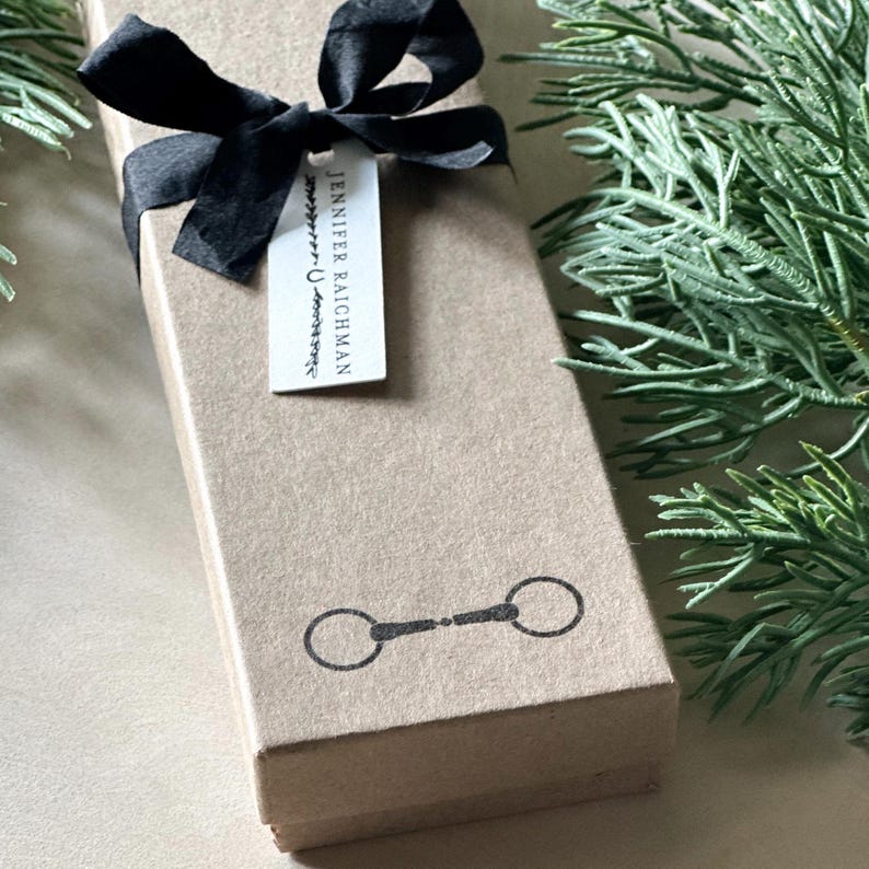 May include: A brown gift box with a black ribbon and a gift tag that says "Jennifer Raichman". The box has a black and white image of a horse bit on the front.