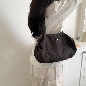 Puede incluir: Un bolso tote con estampado de leopardo marr&oacute;n y negro con dos asas. El bolso est&aacute; hecho de un material suave y tiene un cierre de bot&oacute;n. El bolso se lleva al hombro.