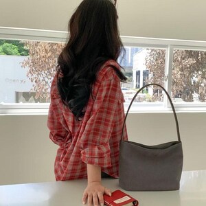 May include: A red plaid shirt with a gray handbag and a small red notebook. The handbag has a curved handle and a rectangular shape. The notebook is open, revealing white pages. The shirt is red with a white grid pattern.