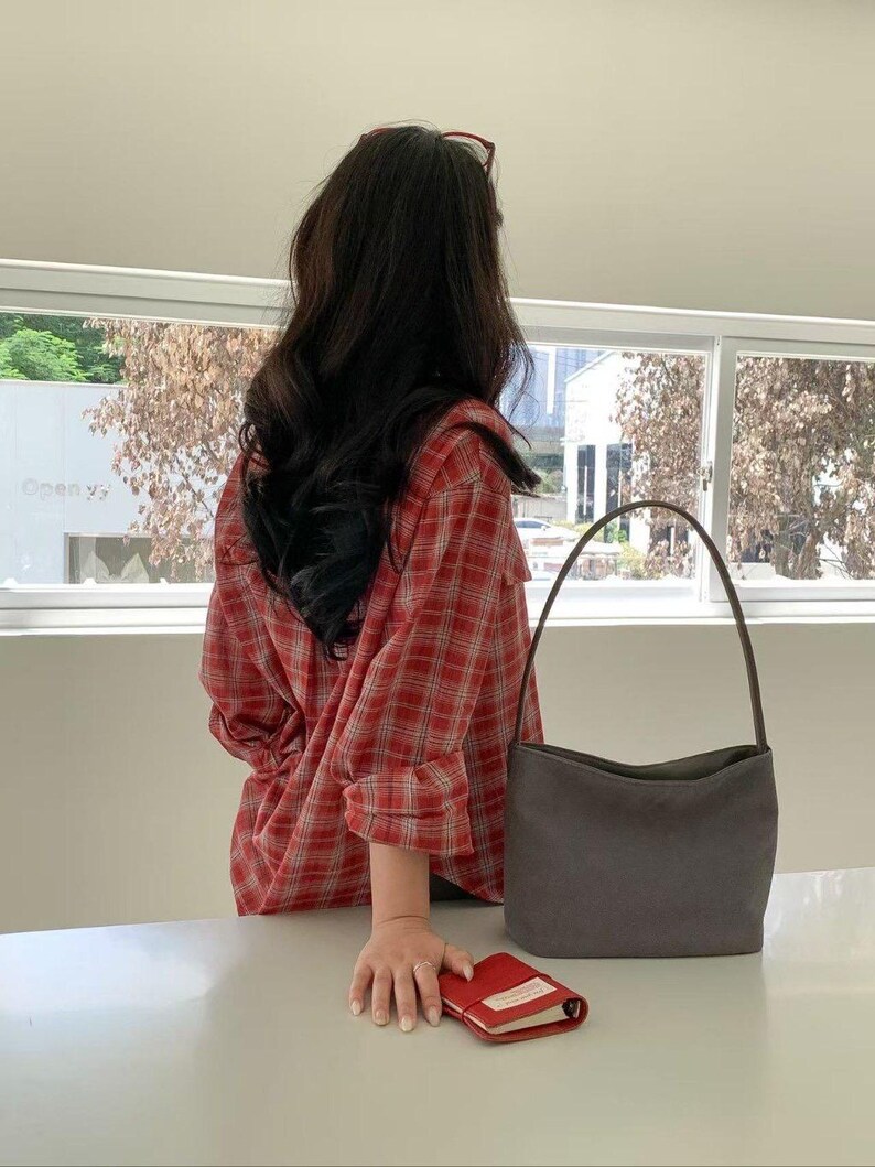 May include: A red plaid shirt with a gray handbag and a small red notebook. The handbag has a curved handle and a rectangular shape. The notebook is open, revealing white pages. The shirt is red with a white grid pattern.