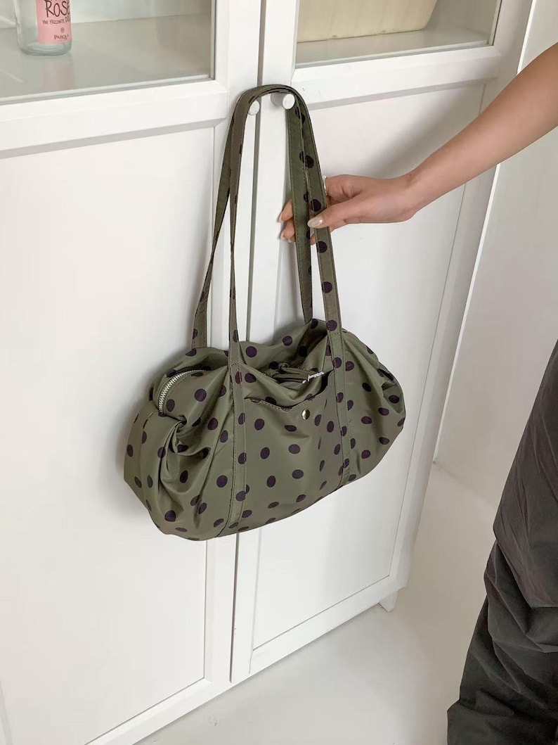 Puede incluir: Bolso tote verde oliva con lunares morados oscuros. El bolso tiene dos asas largas y una cremallera en la parte superior. Un peque&ntilde;o bolsillo es visible en la parte delantera del bolso.
