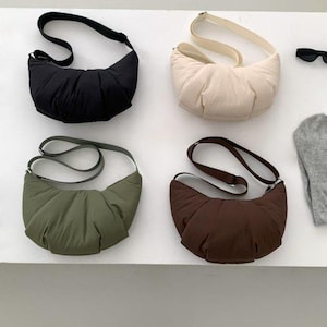 Peut inclure: Quatre sacs à bandoulière en forme de croissant, noirs, crème, vert olive et marron. Chaque sac est doté d'une bandoulière réglable. Les sacs sont en matière matelassée souple.