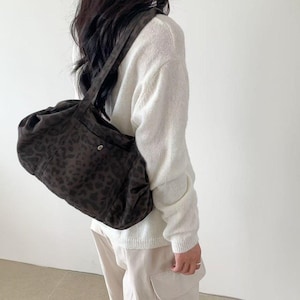 Puede incluir: Un bolso de hombro marr&oacute;n oscuro con estampado de leopardo. El bolso se lleva sobre el hombro. La persona lleva un su&eacute;ter blanco y pantalones color beige.