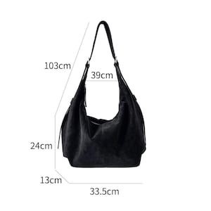 May include: Black suede shoulder bag with a single strap. The bag is 103cm long, 39cm wide, 24cm high, and 13cm deep. The base of the bag is 33.5cm wide. The bag has a simple, minimalist design.