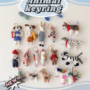 May include: A collection of 16 felt animal keychains, including a dog, rabbit, pig, bear, zebra, unicorn, llama, and sloth. The keychains are all different colours and have various details, such as a beach ball, a surfboard, a carrot, and a scarf. The keychains are arranged in a circle on a white background. The text "NEW!" is in a starburst shape in the bottom left corner of the image.