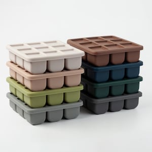 Könnte beinhalten: Ein Stapel aus neun Silikon-Eiswürfelformen in verschiedenen Farben, darunter Grau, Grün, Braun, Rosa und Weiß. Die Formen sind alle quadratisch und haben neun einzelne Fächer für Eiswürfel.