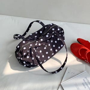 Puede incluir: Bolso de viaje negro con lunares blancos, con cierre de cremallera y dos asas. La bolsa est&aacute; hecha de un material ligero. Zapatos rojos y libros en el fondo.