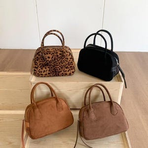 Puede incluir: Cuatro bolsos pequeños en diferentes colores y texturas. Un bolso tiene un estampado de leopardo, otro es negro y los otros dos son tonos marrones. Cada bolso tiene forma redondeada, cierre de cremallera y dos asas.
