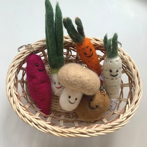 Puede incluir: Una cesta de mimbre llena de llaveros de comida de fieltro. Los llaveros tienen forma de zanahoria, champiñón, cebolla, patata y un objeto redondo marrón. Cada llavero tiene una cara sonriente.