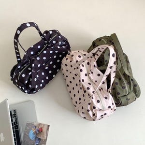 Puede incluir: Tres peque&ntilde;os bolsos cil&iacute;ndricos con asas y cremalleras. Uno es negro con lunares blancos, otro rosa claro con lunares negros y el tercero verde oliva con lunares negros. Un port&aacute;til y una peque&ntilde;a foto est&aacute;n en la esquina inferior izquierda.