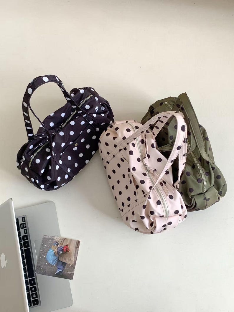 Puede incluir: Tres peque&ntilde;os bolsos cil&iacute;ndricos con asas y cremalleras. Uno es negro con lunares blancos, otro rosa claro con lunares negros y el tercero verde oliva con lunares negros. Un port&aacute;til y una peque&ntilde;a foto est&aacute;n en la esquina inferior izquierda.