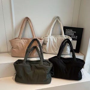 Peut inclure: Quatre sacs fourre-tout de couleurs rose blush, blanc cassé, vert olive et noir. Chaque sac a un design gonflé et des poignées assorties. Un panneau noir et blanc avec du texte est en arrière-plan.