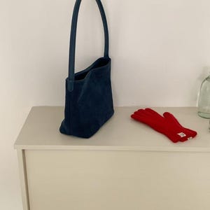 May include: A navy blue tote bag with a long handle and a pair of red gloves. The bag is made of a soft material and has a simple design. The gloves are made of a warm material.