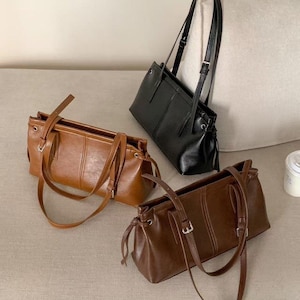 Peut inclure: Trois sacs à main rectangulaires de différentes nuances de marron et de noir. Chaque sac est doté d'une longue bandoulière réglable et d'une poignée supérieure. Les sacs sont fabriqués dans un matériau lisse et présentent un design simple et élégant.