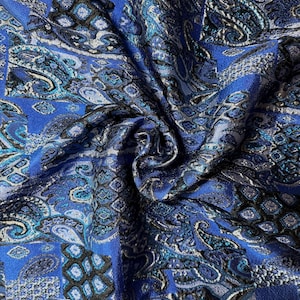 Op de afbeelding: Close-up van een levendige blauwe stof met een paisley patroon. Het ontwerp bevat tinten blauw, blauwgroen en zwart, waardoor een textuur en gedetailleerd uiterlijk ontstaat. De stof wordt waarschijnlijk gebruikt voor kleding of woondecoratie.