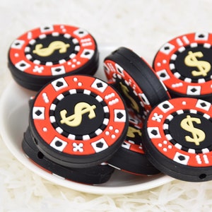 May include: A group of six black and red silicone casino chip-shaped beads with a gold dollar sign on each. The beads are on a white surface.