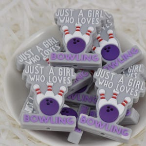May include: A collection of gray and purple silicone charms with the text "Just a girl who loves bowling" and a bowling pin and ball graphic.