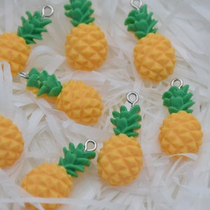 Puede incluir: Un conjunto de ocho abalorios de piña amarillos y verdes con anillas de salto plateadas. Los abalorios están hechos de plástico y tienen un diseño de piña realista.