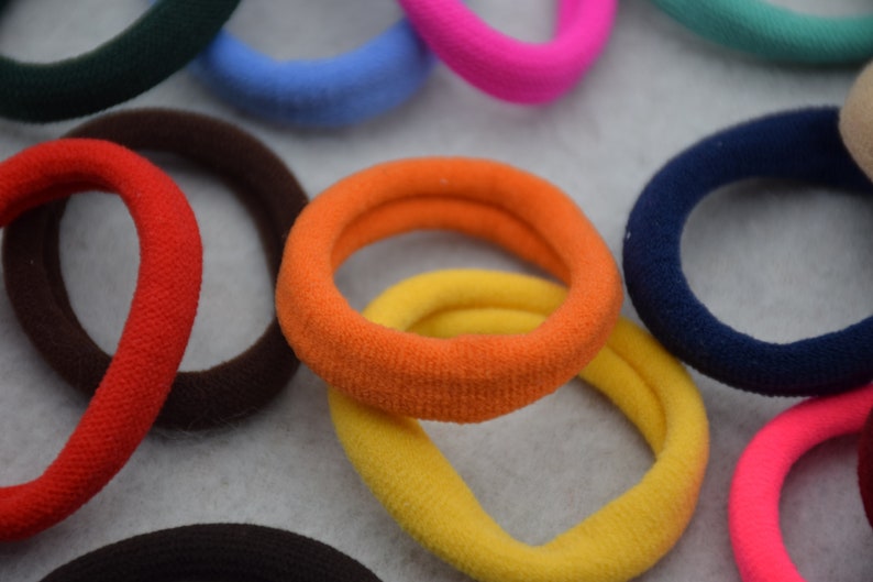 May include: Assortment of colorful hair ties in various shades of blue, red, orange, yellow, pink, green, and brown. The hair ties are made of soft, stretchy fabric and are perfect for holding back hair.
