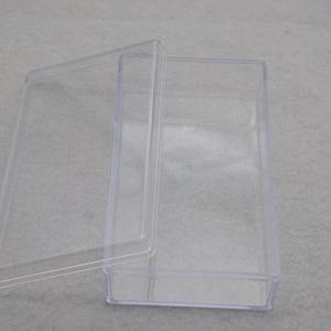 May include: A clear plastic rectangular box with a lid. The box is empty and the lid is open.