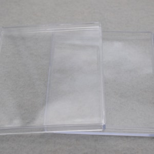 May include: Two clear plastic boxes, one slightly larger than the other, are stacked on top of each other. The boxes are empty and have a smooth, glossy finish.