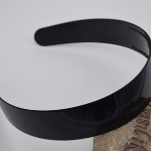 May include: A black plastic headband with a glossy finish. The headband is curved and has a smooth surface.