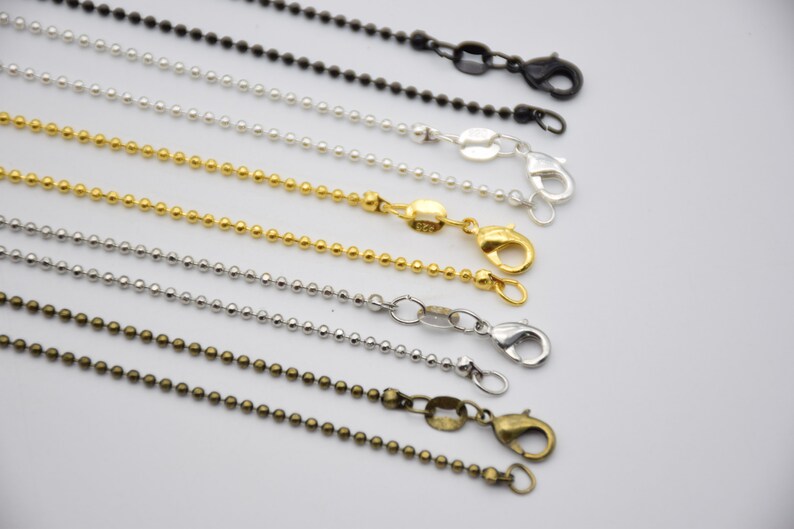 May include: Assortment of ball chain necklaces in silver, gold, and bronze finishes. Each chain features a lobster clasp closure.