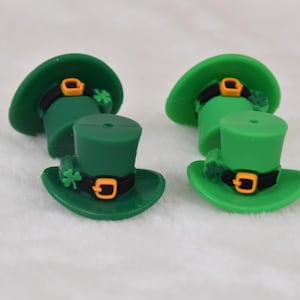 May include: Four green leprechaun hats with black bands, gold buckles, and shamrock accents. The hats are made of a soft, pliable material.