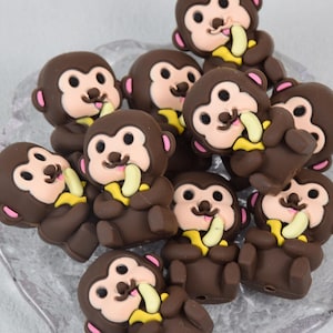 May include: A collection of brown chocolate monkey-shaped candies with yellow banana accents. Each monkey is holding a banana in its hand and has a pink mouth.