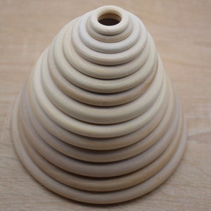 Könnte beinhalten: Ein Holz-Stapelspielzeug in Form eines Kegels. Das Spielzeug ist aus Naturholz gefertigt und hat eine glatte Oberfläche. Die Ringe sind nach Größe gestapel, wobei der größte Ring unten und der kleinste Ring oben liegt.