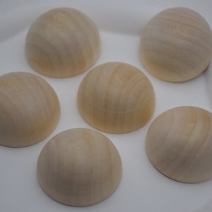 Peut inclure: Six demi-sphères en bois non finies, chacune avec une surface lisse de couleur brun clair. Les sphères sont disposées en cercle sur un fond blanc.