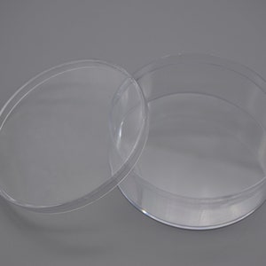 May include: Two clear plastic round containers with lids. The lids are off and the containers are sitting on a grey surface.