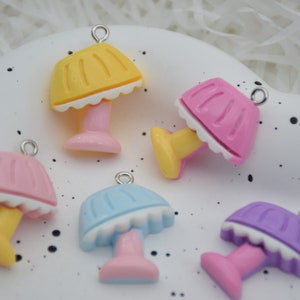 May include: Five colorful plastic lamp charms with white trim. The charms are yellow, pink, blue, and purple. Each charm has a silver loop for hanging.