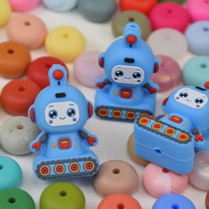 May include: A collection of colorful silicone beads and blue robot-shaped charms. The robot charms have a cute face and are decorated with red and orange accents. The beads are in various colors, including pink, yellow, and green.