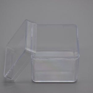 May include: A clear plastic square box with a lid. The box is empty and the lid is slightly ajar.